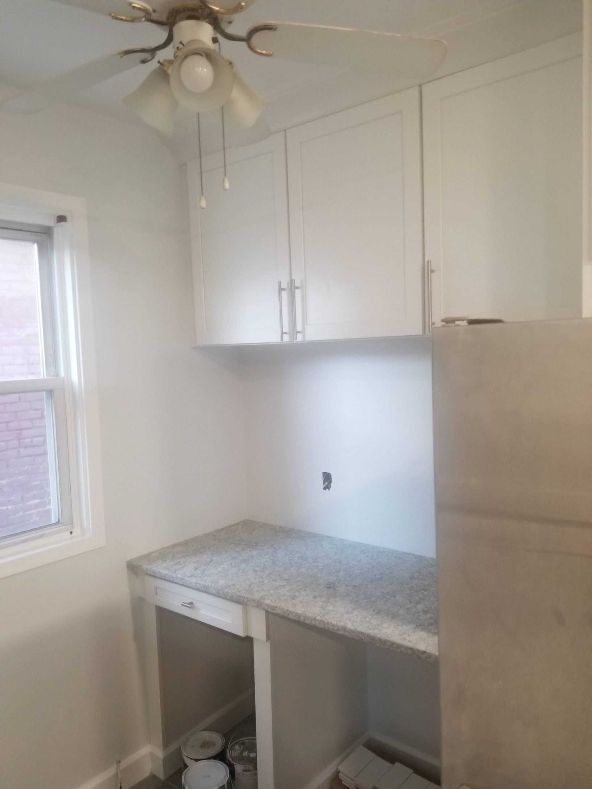 A kitchen with white cabinets, a granite counter top, a refrigerator and a ceiling fan.