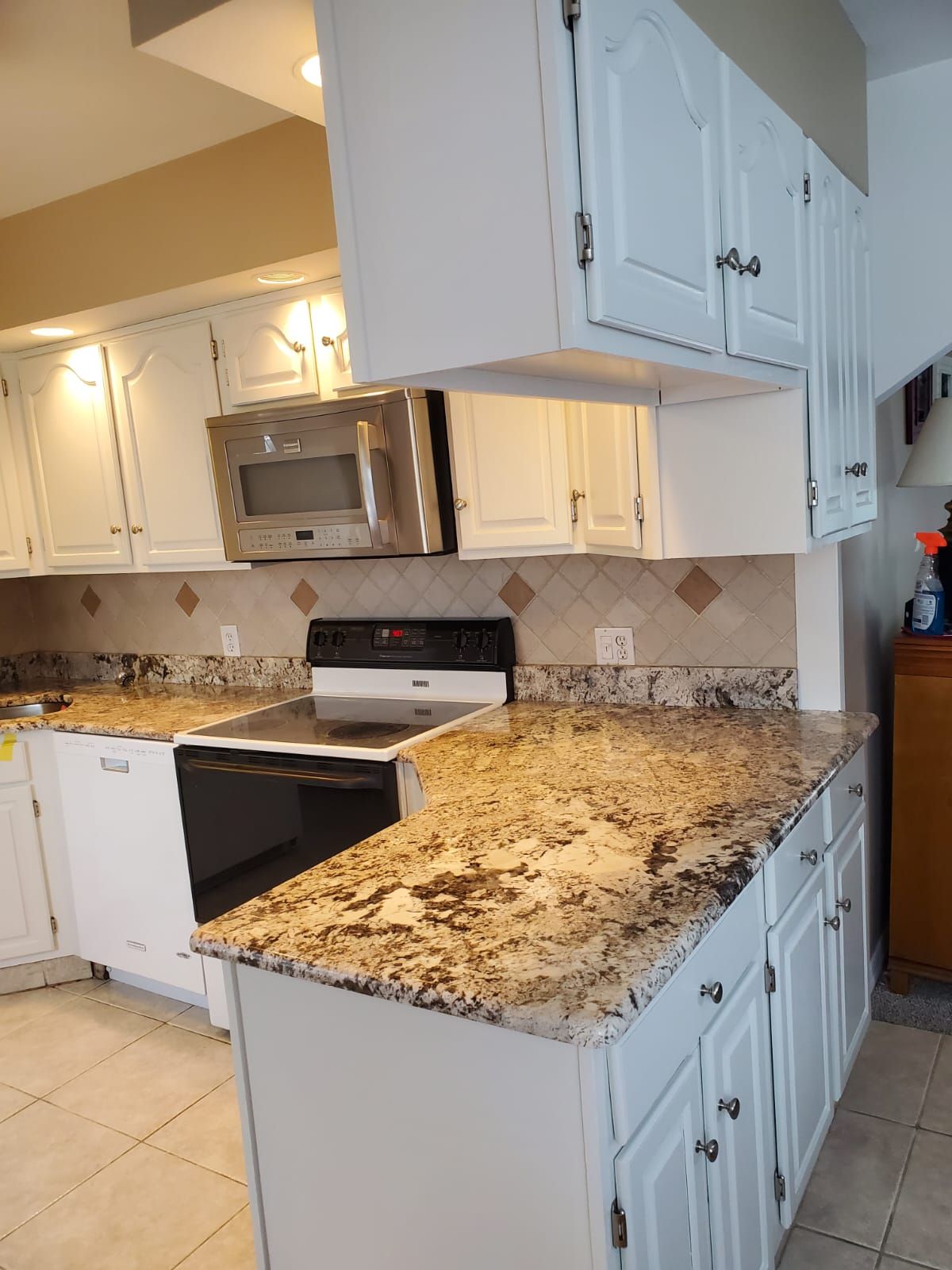 A kitchen with granite counter tops, white cabinets, a stove and a microwave.