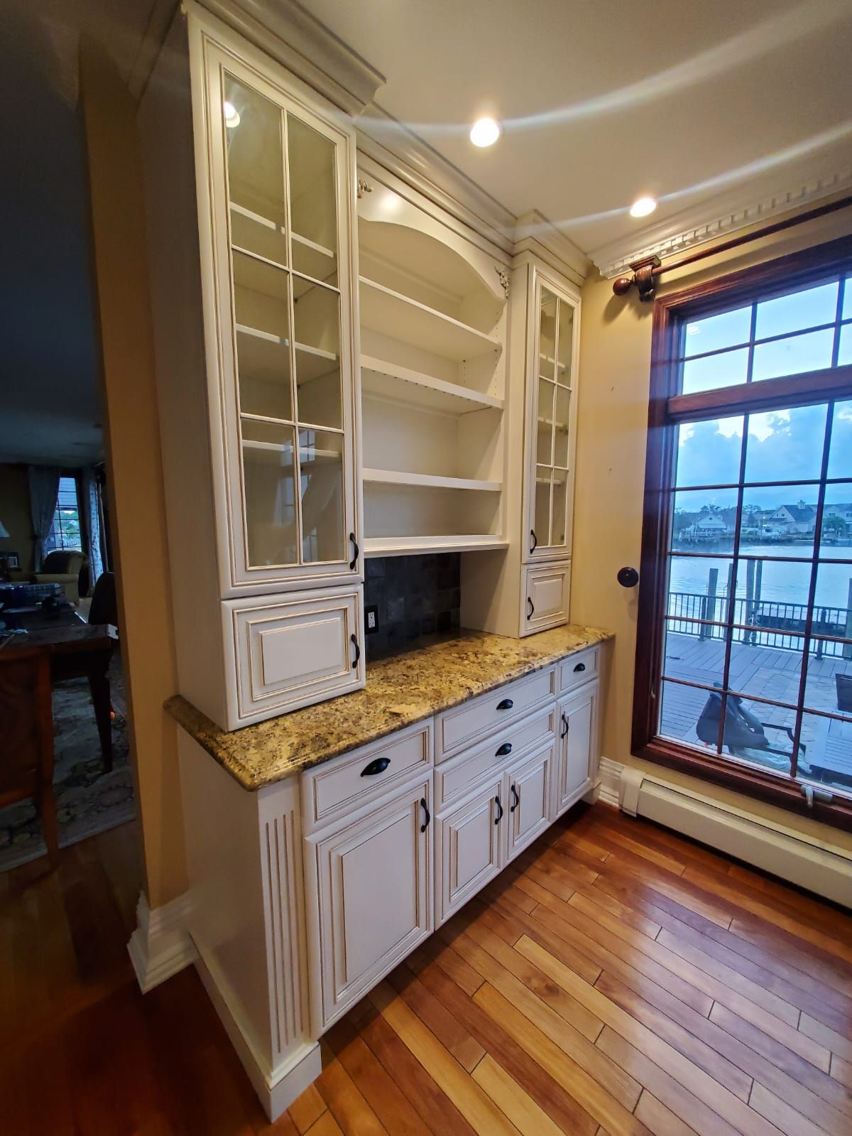 A kitchen with white cabinets, granite counter tops, and a large window.