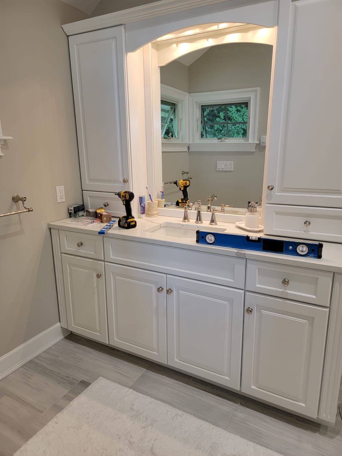 A bathroom with white cabinets , a sink and a mirror.
