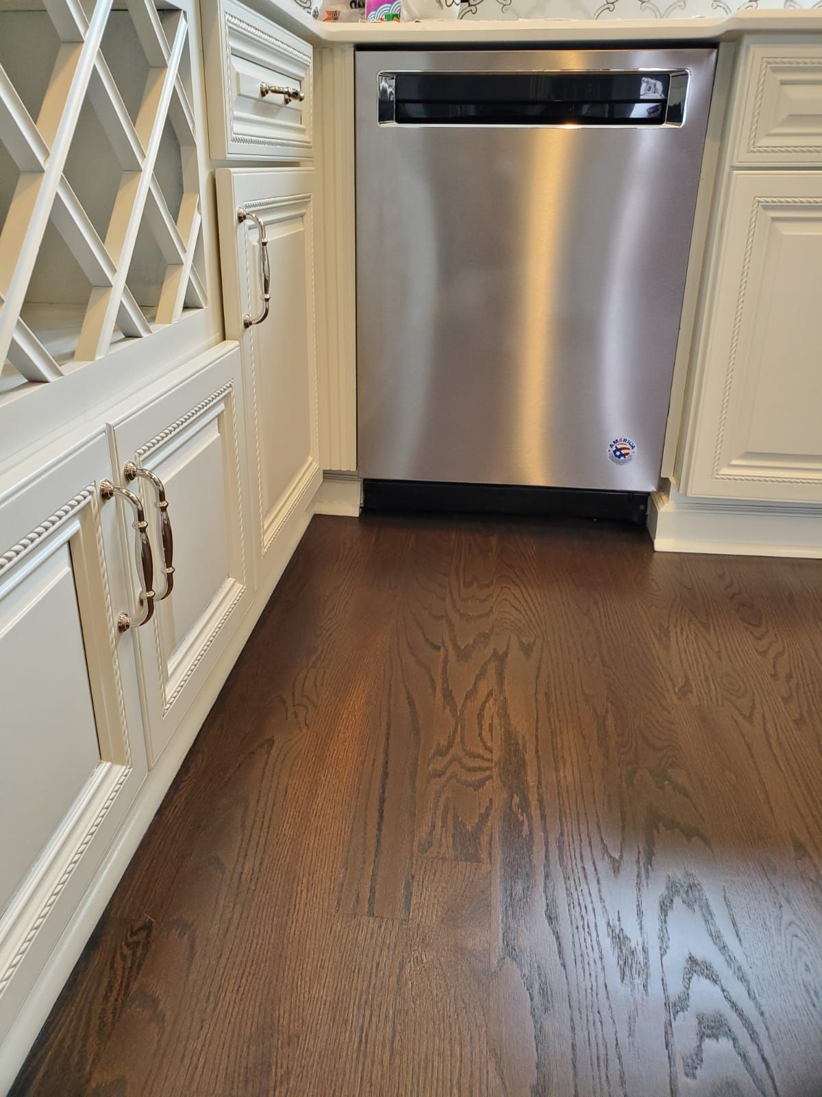 A stainless steel dishwasher is sitting in a kitchen next to a wine rack.