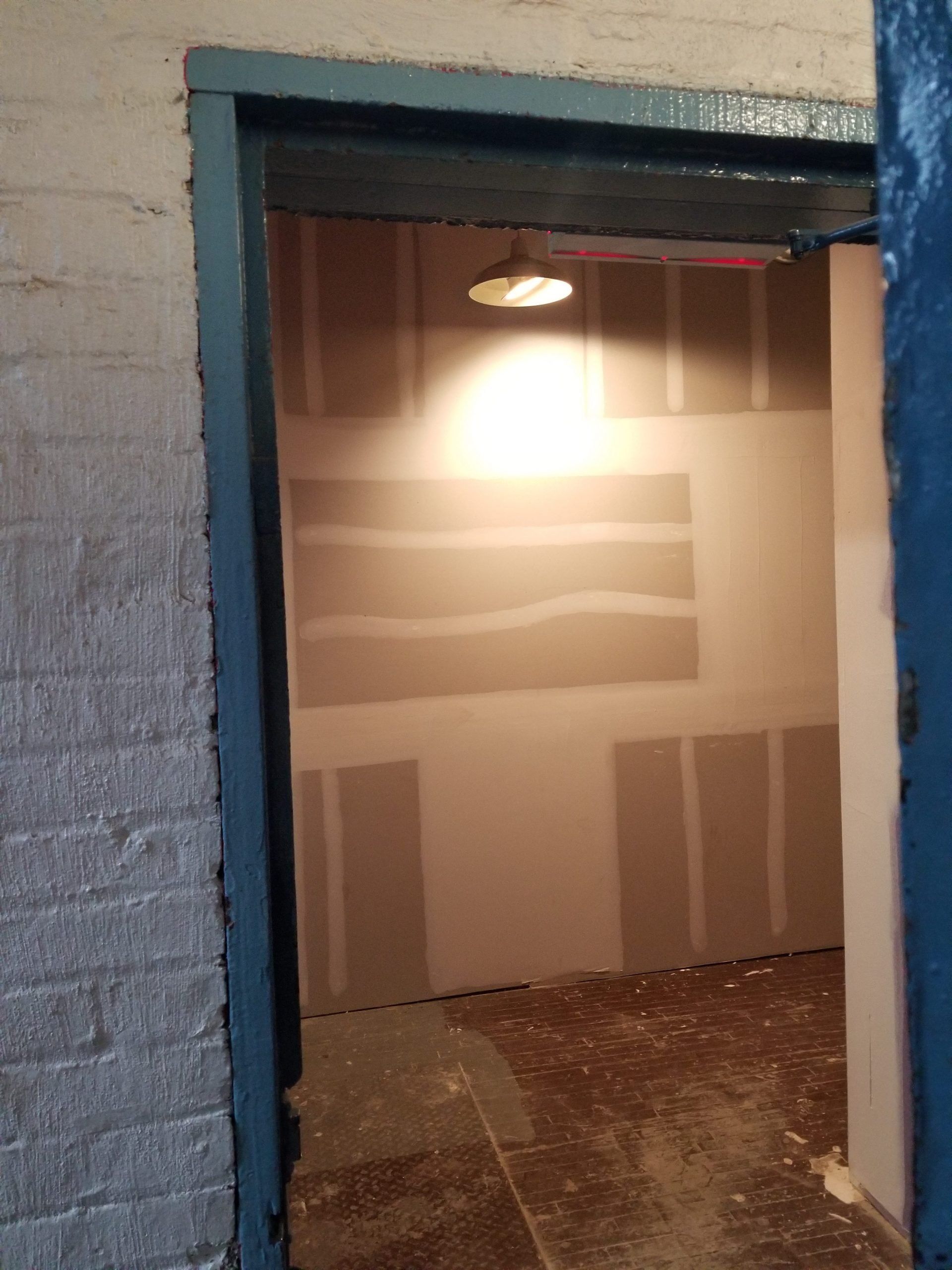 An empty room with a blue door and a light on the ceiling.