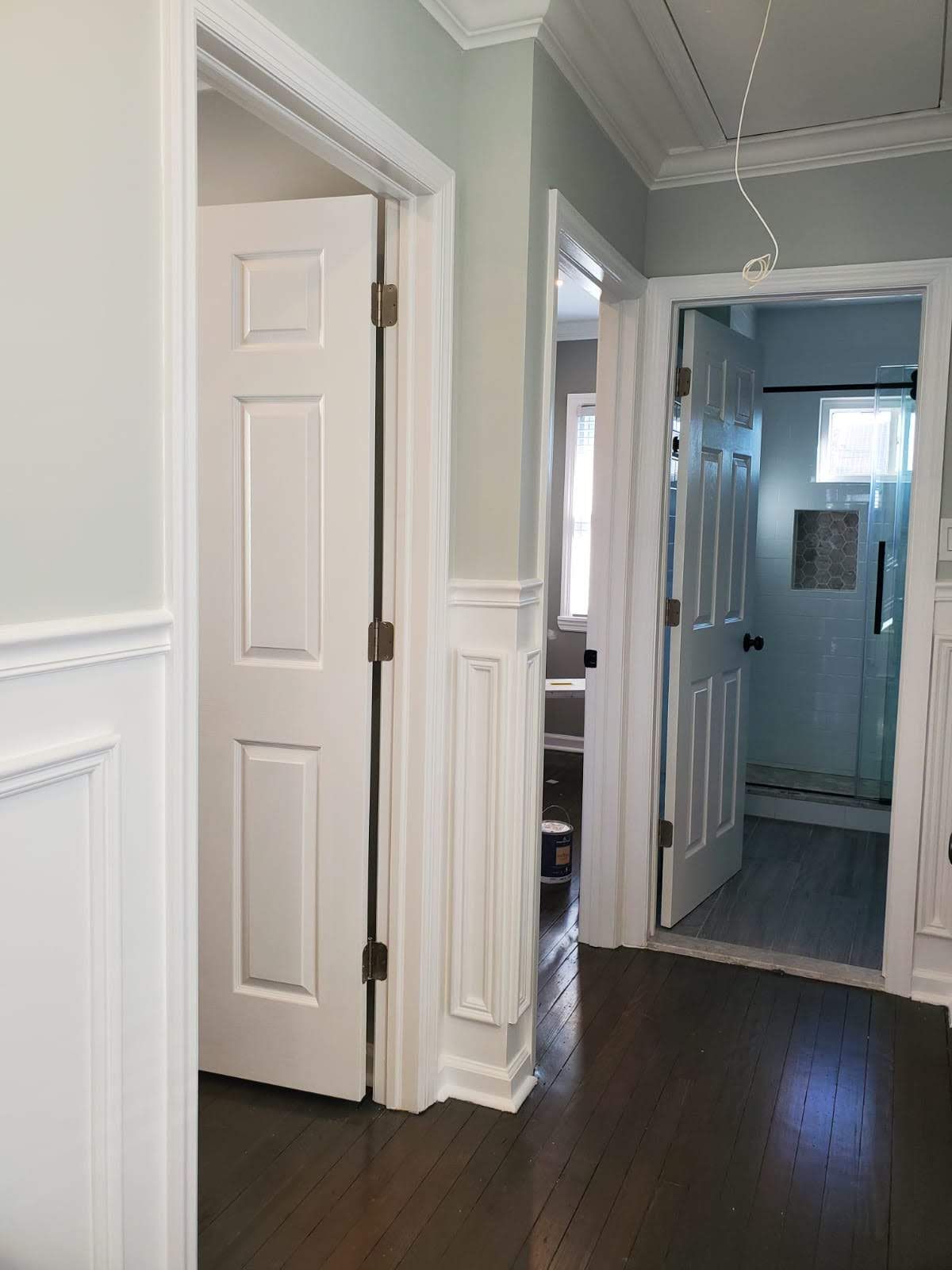 A hallway with white walls and hardwood floors leading to a bathroom.
