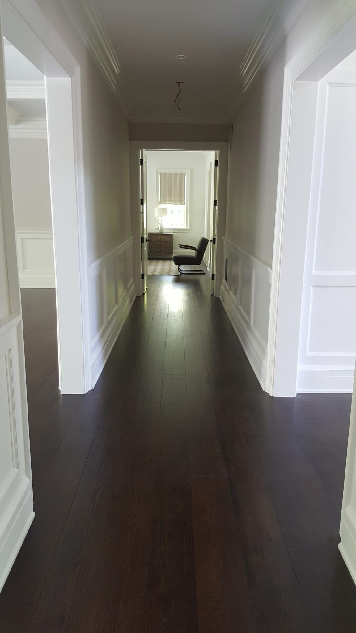 A long hallway with dark wood floors and white trim leading to a living room.