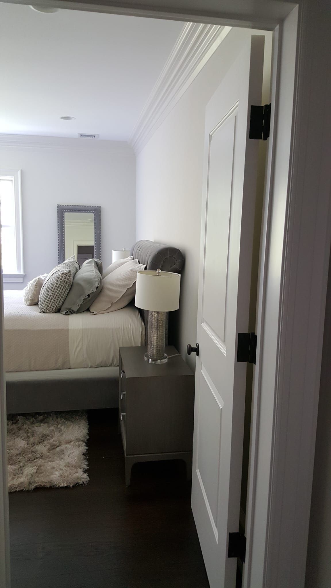 A bedroom with a bed, nightstand, lamp and mirror.