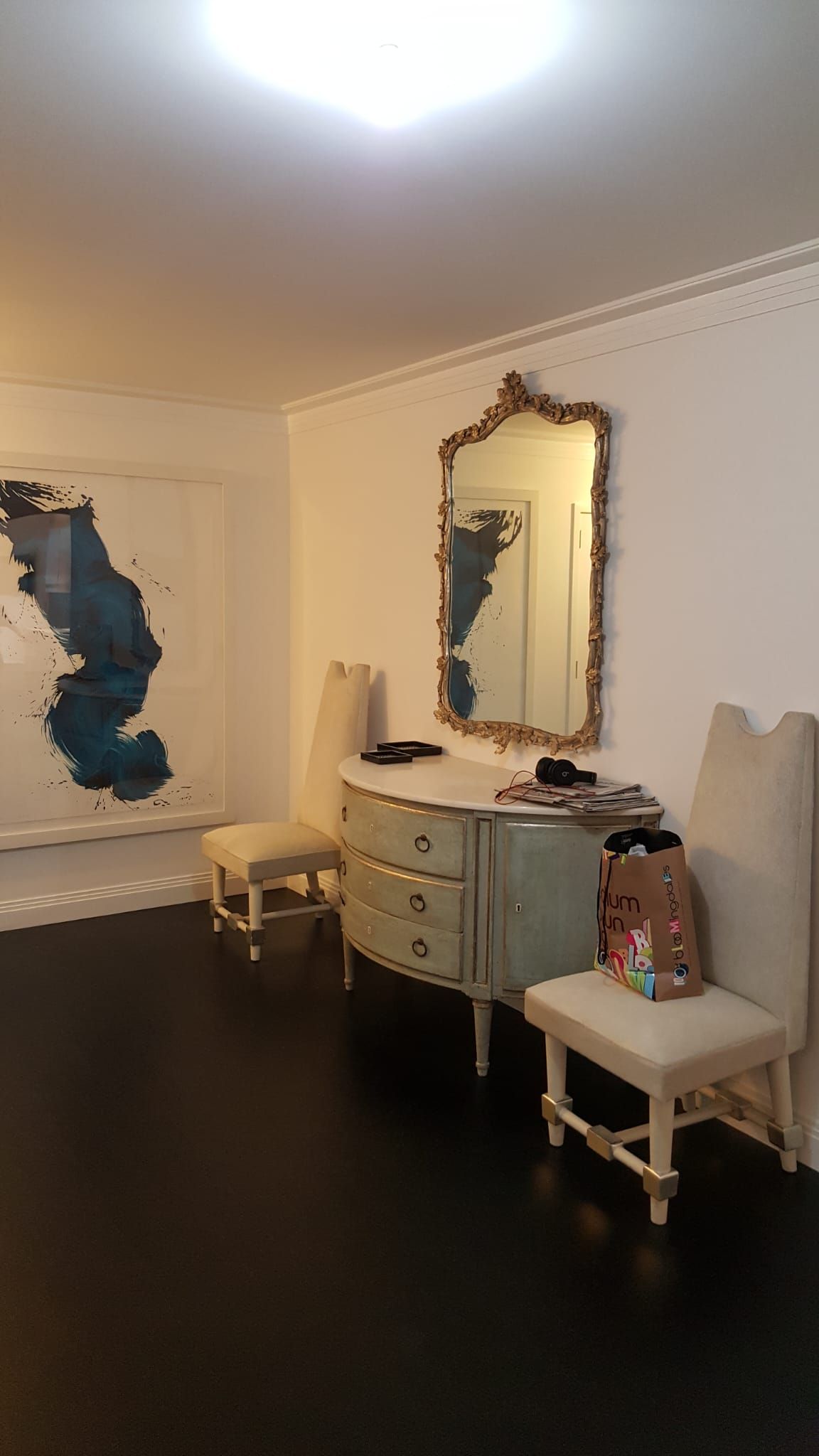 A room with a dresser, chairs, a mirror and a painting on the wall.