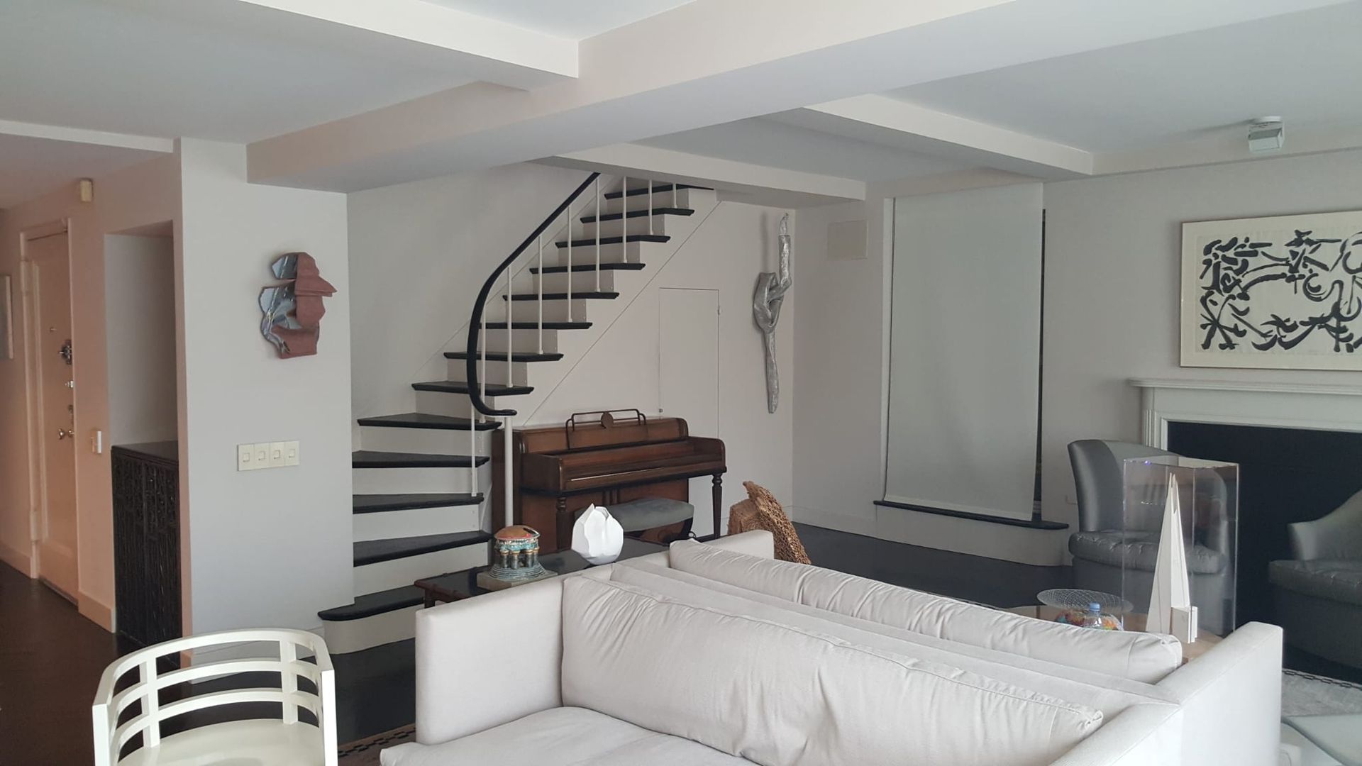 A living room with a couch, chairs, stairs and a fireplace.