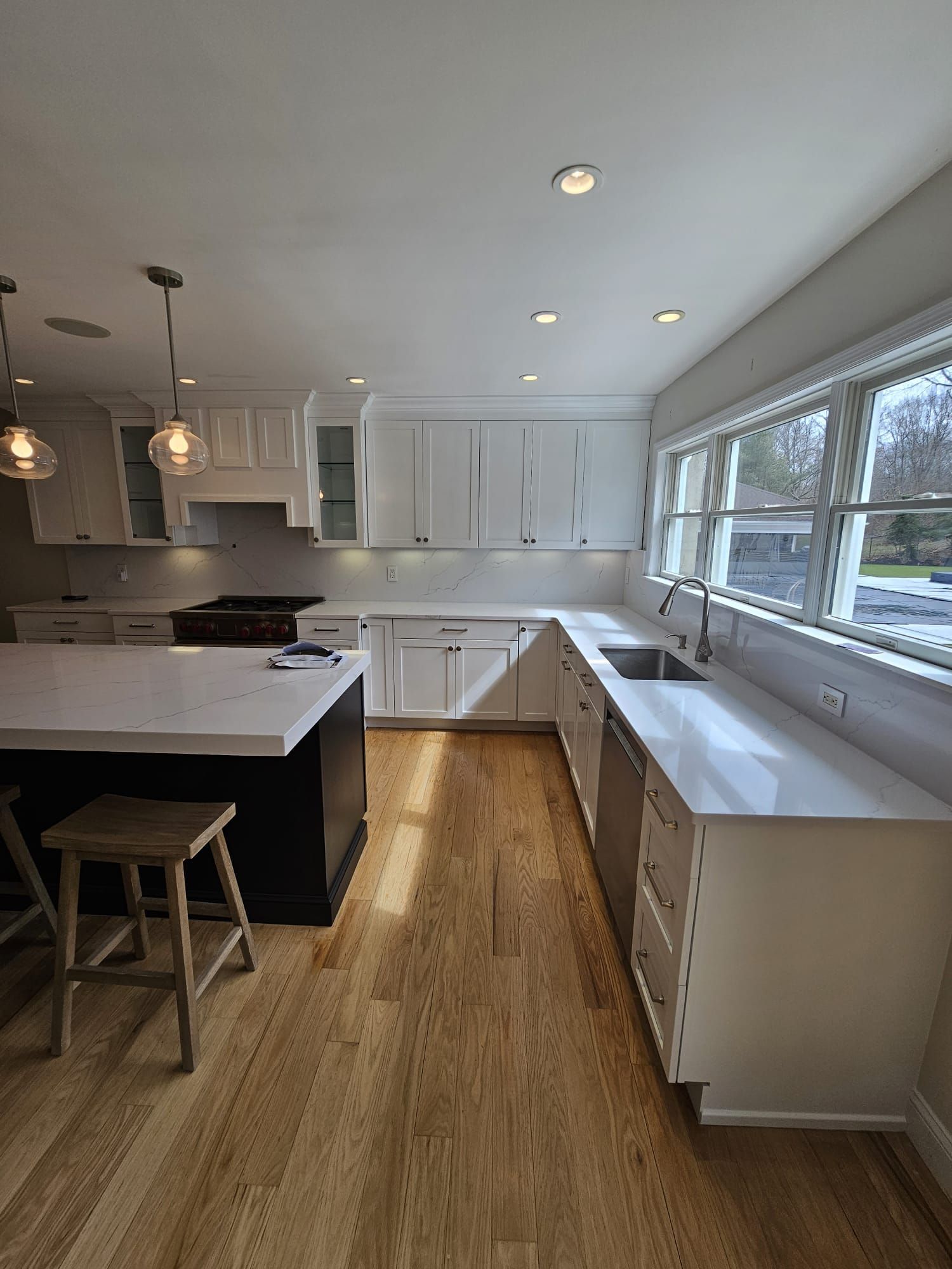 A kitchen with white cabinets, hardwood floors, a sink, and a large island.