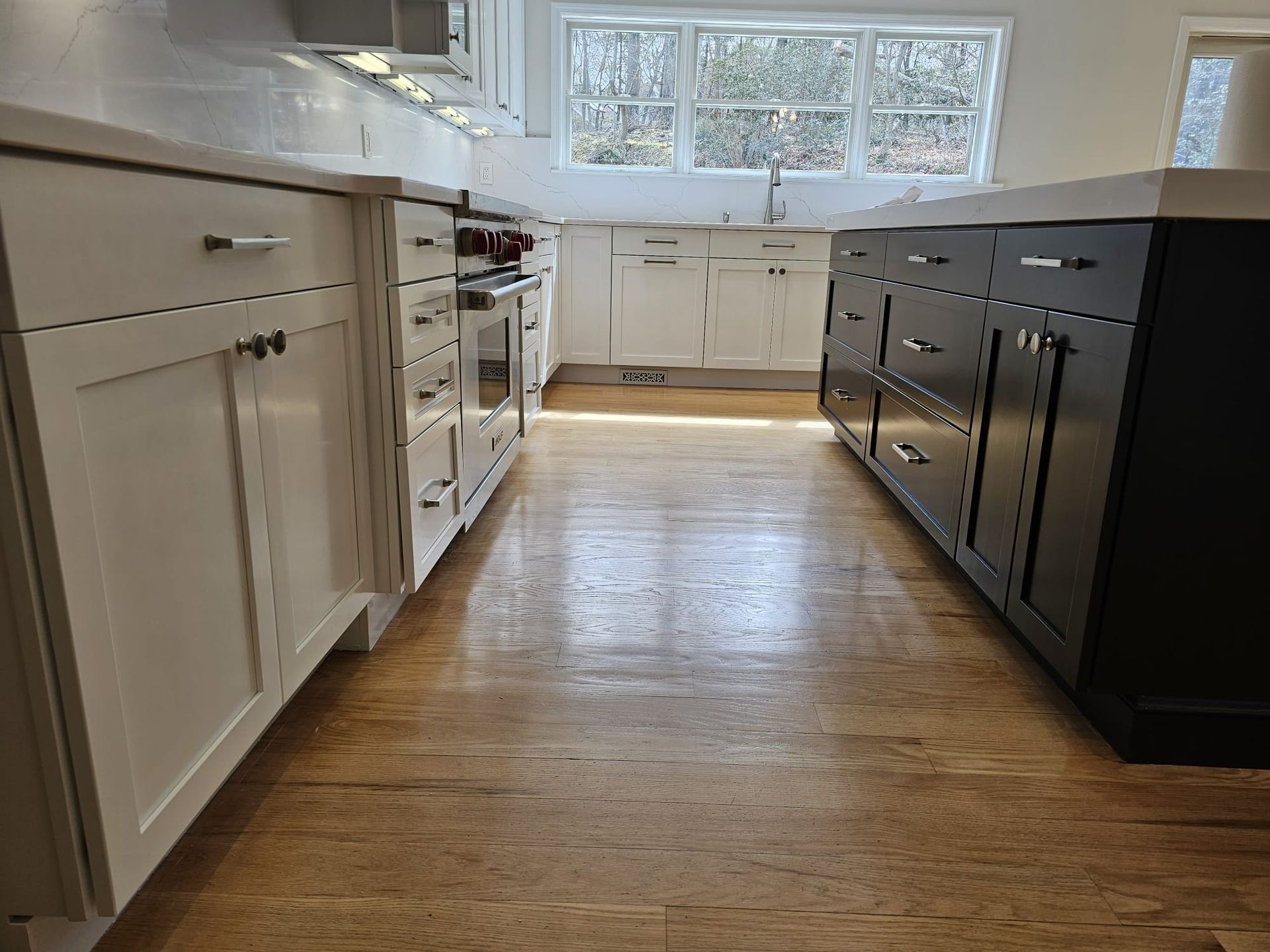 A kitchen with white cabinets and black drawers and a wooden floor.
