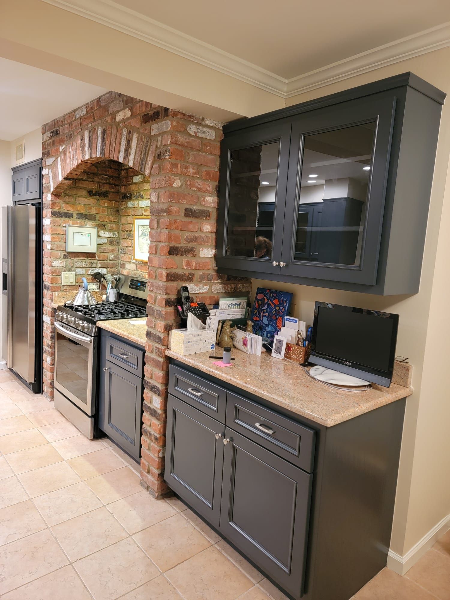 A kitchen with gray cabinets, a stove, a refrigerator, and a laptop on the counter.