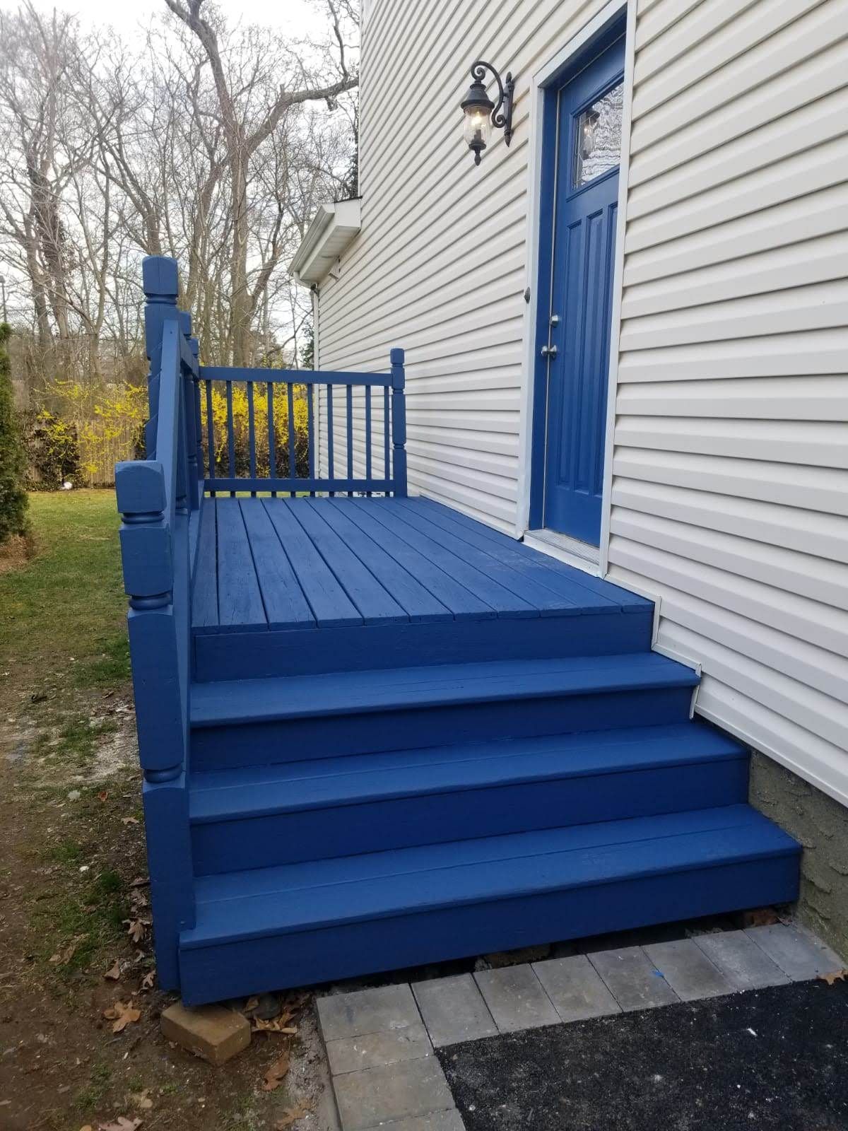 A blue deck with blue stairs is in front of a white house.
