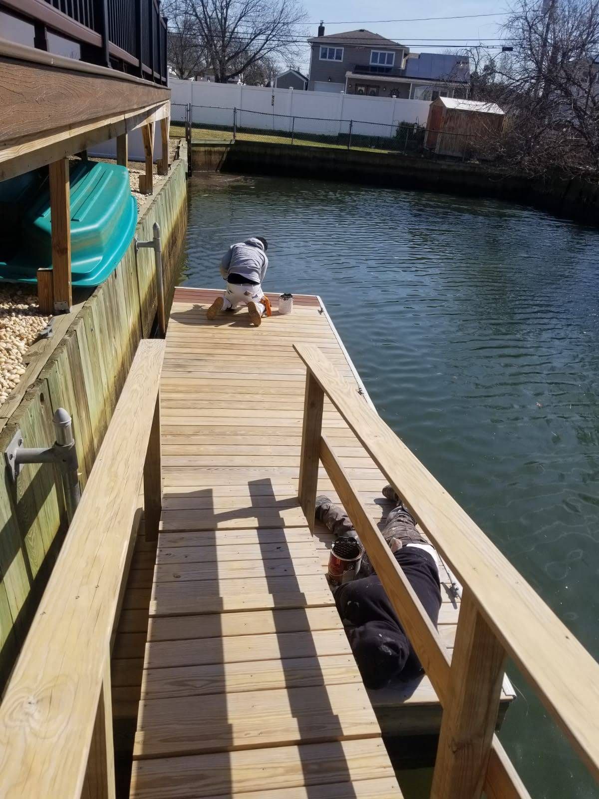 A man is kneeling on a wooden dock overlooking a body of water.