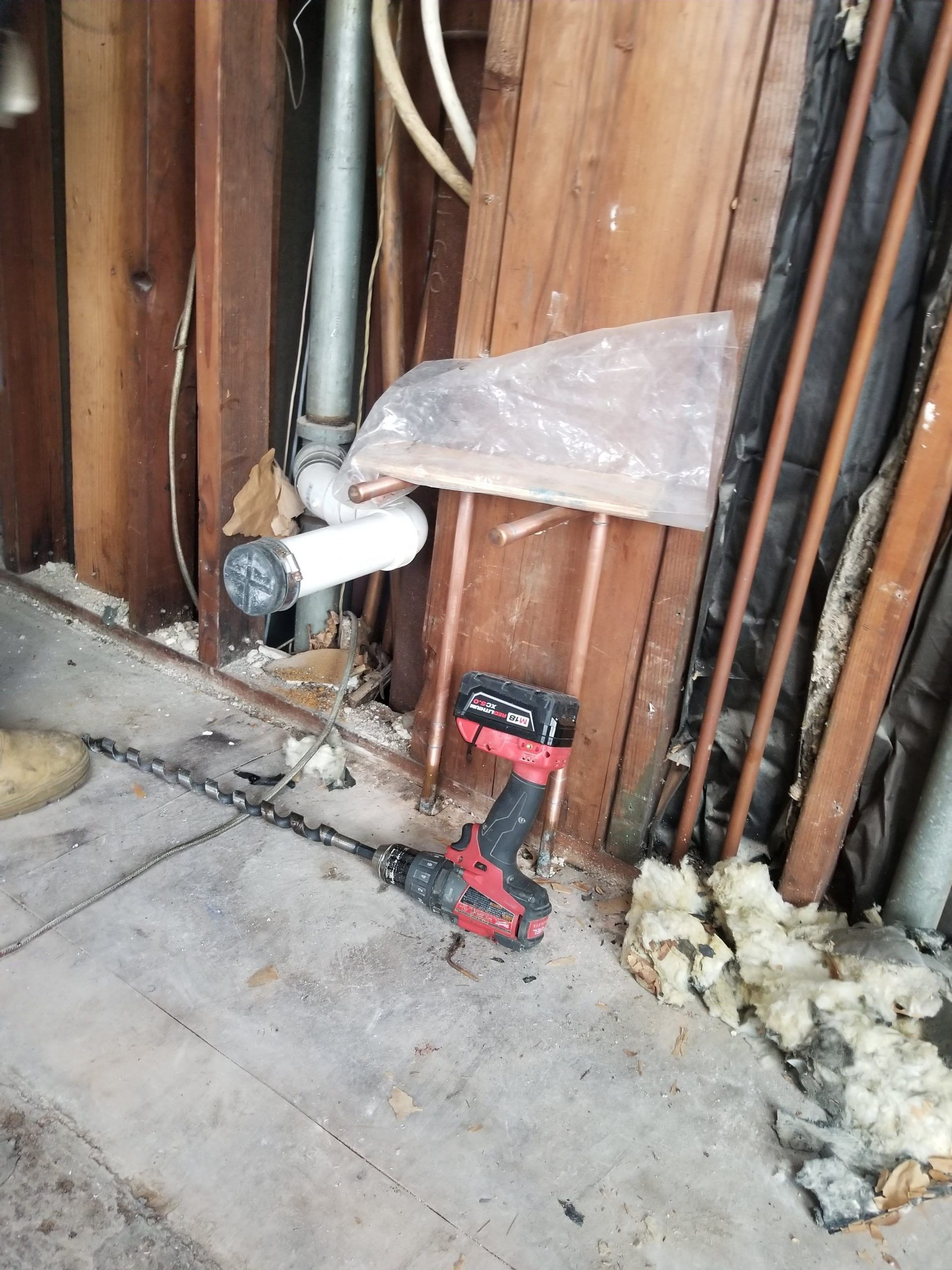 A drill is sitting on the floor next to a wooden wall.