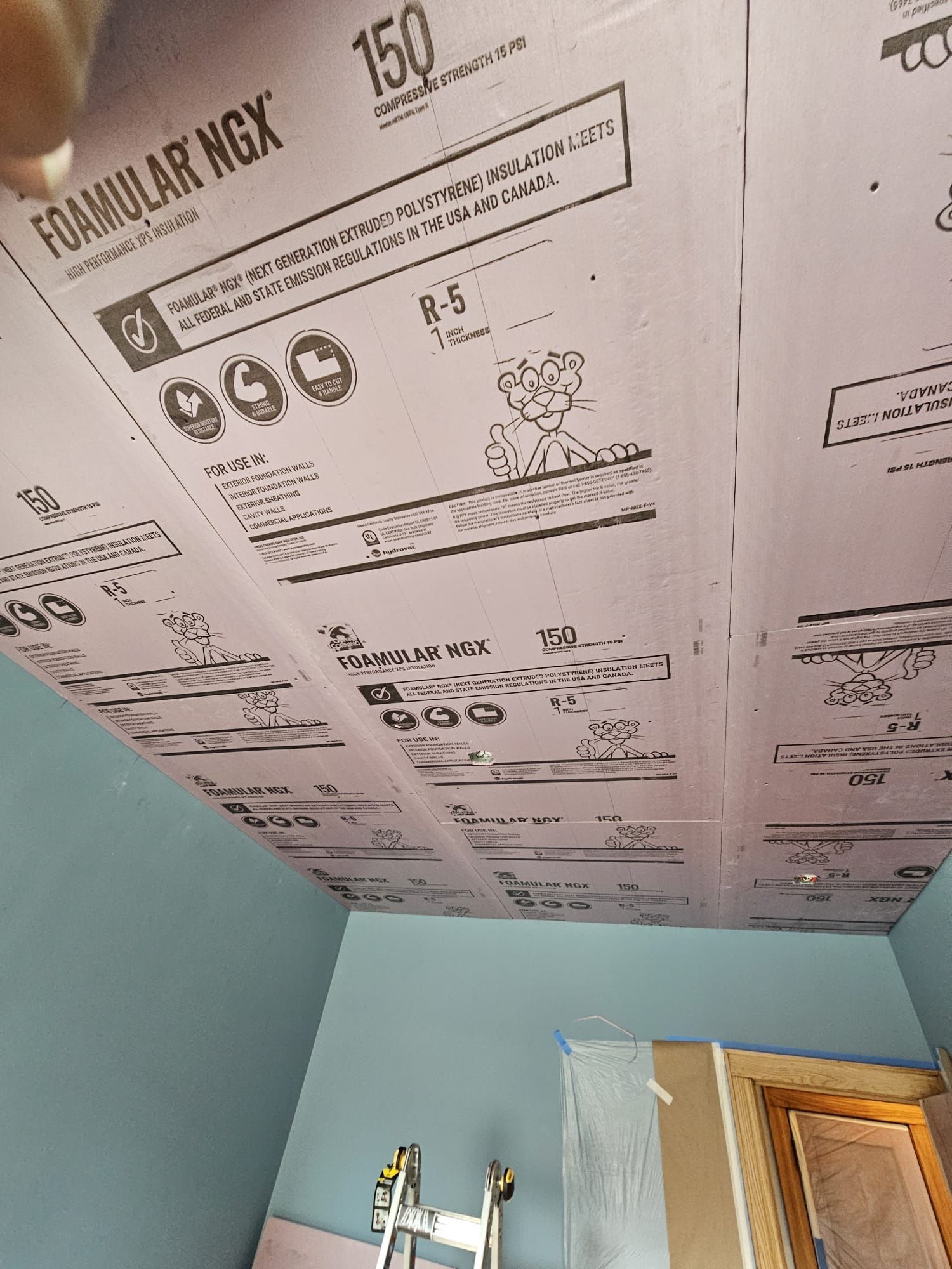 A room with a ladder and foam insulation on the ceiling.
