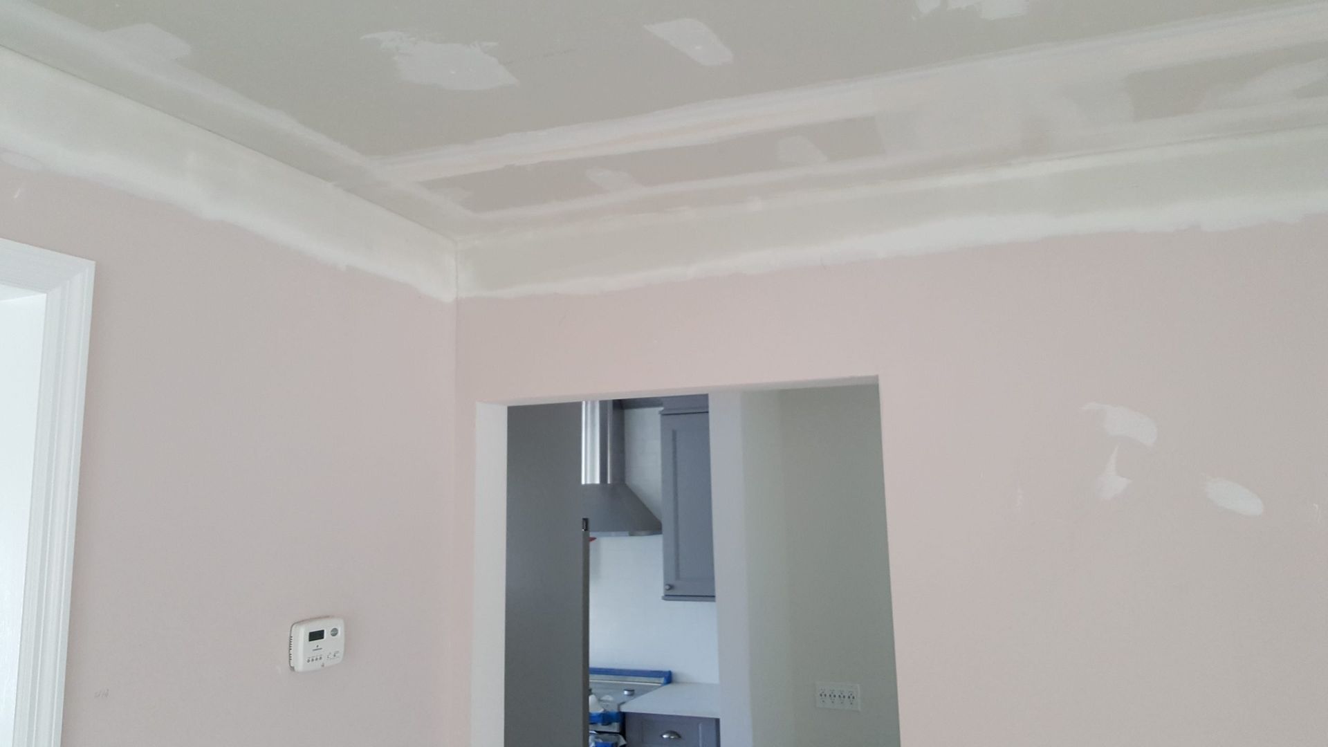 A room with a ceiling that is being painted and a doorway leading to a kitchen.