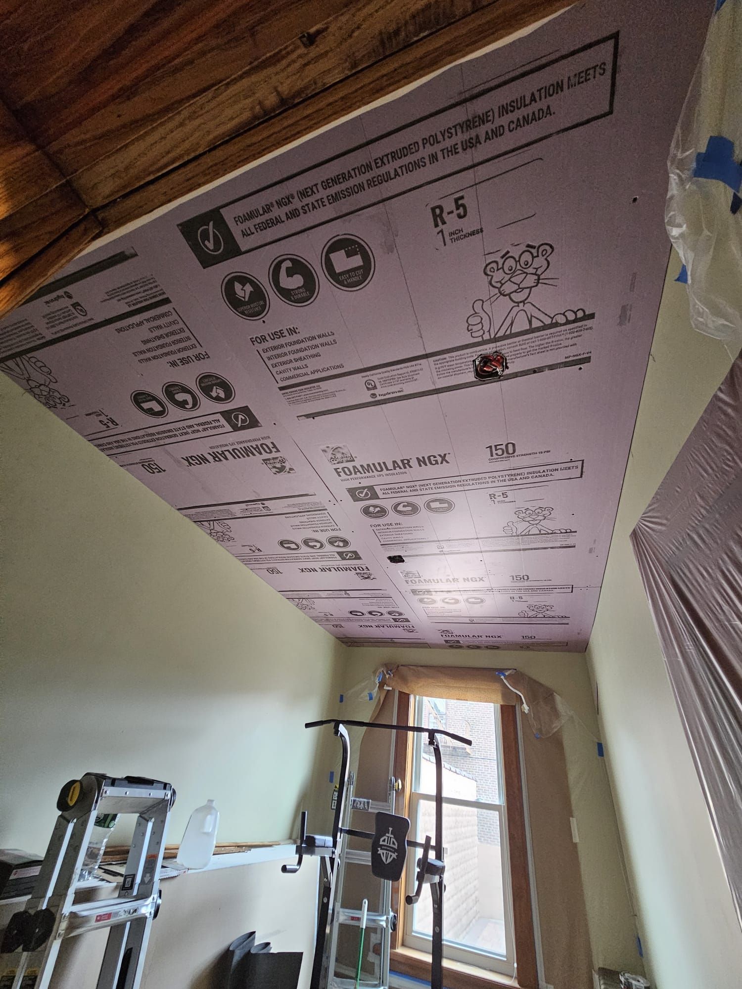 A room with a ladder and a window and a ceiling that is covered in insulation.