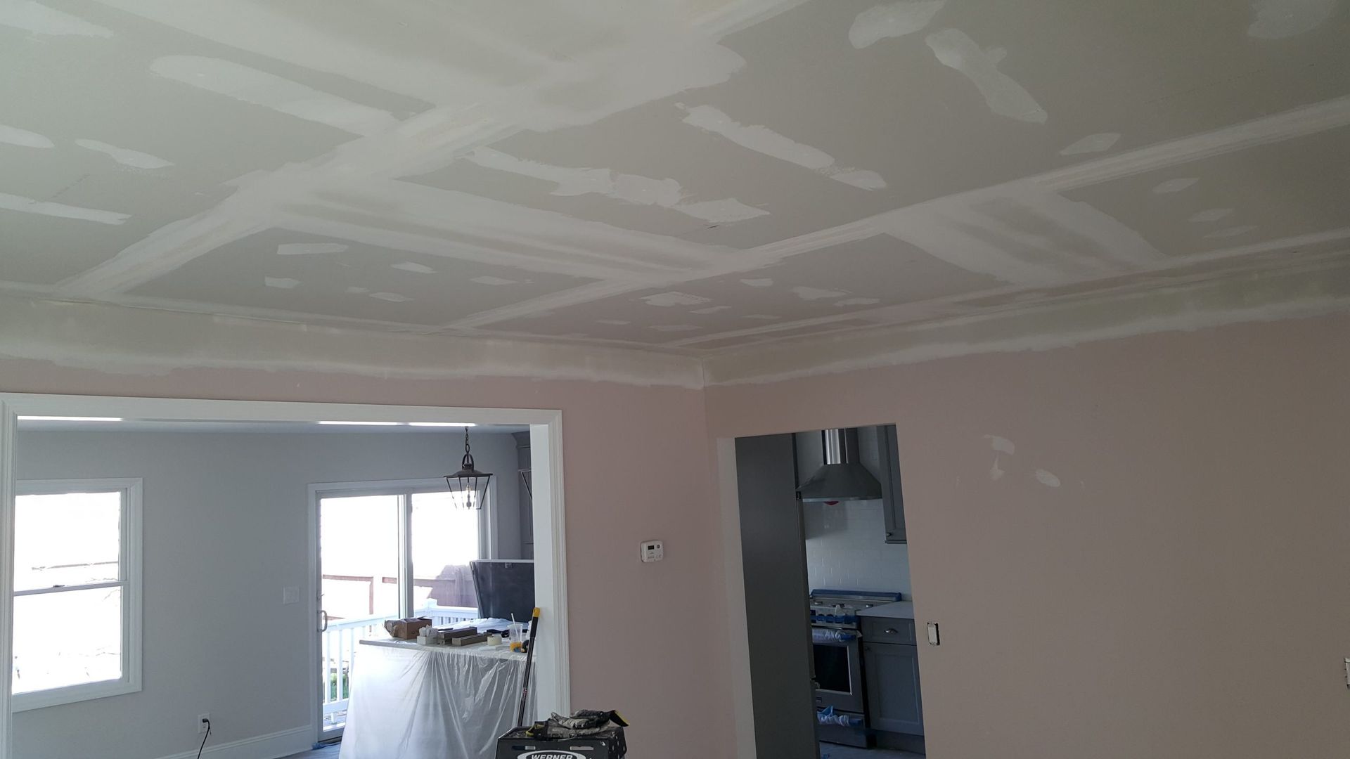 A living room with a ceiling that is being painted and a kitchen in the background.