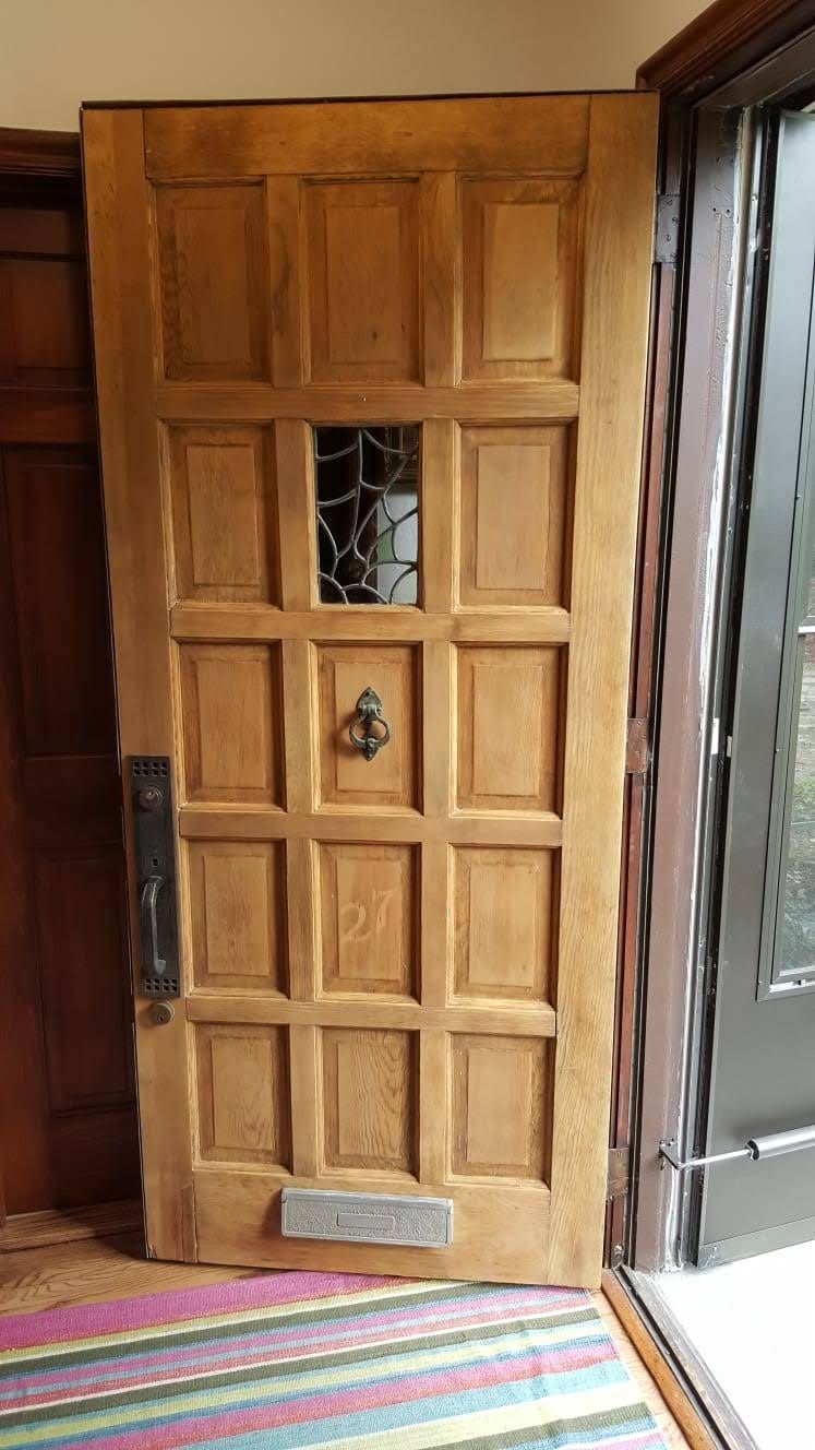 A wooden door with a stained glass window is sitting in a hallway next to a rug.