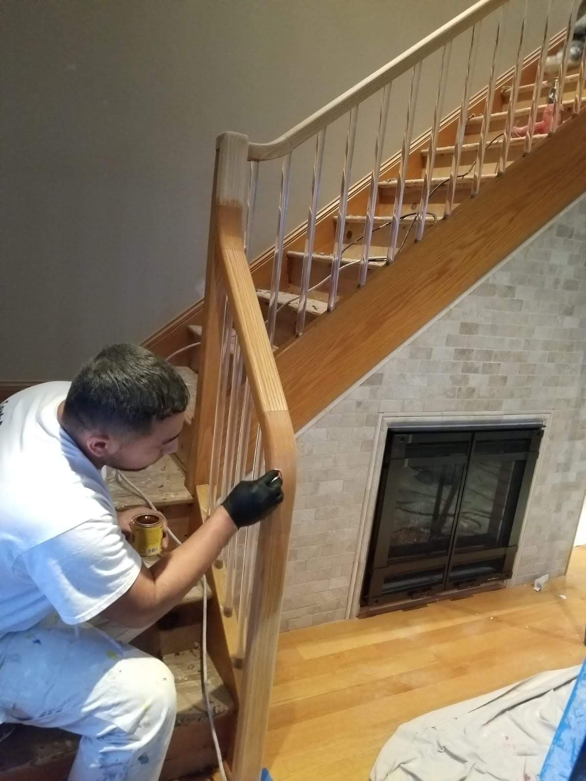 A man is painting a wooden railing on a staircase.