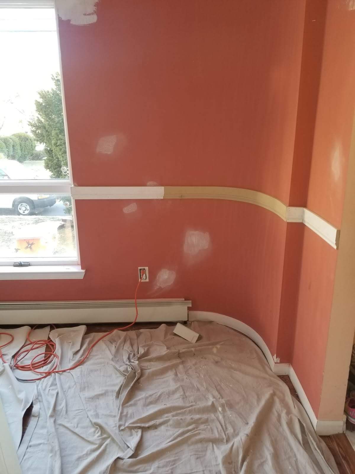 A room with pink walls and a white trim is being painted.