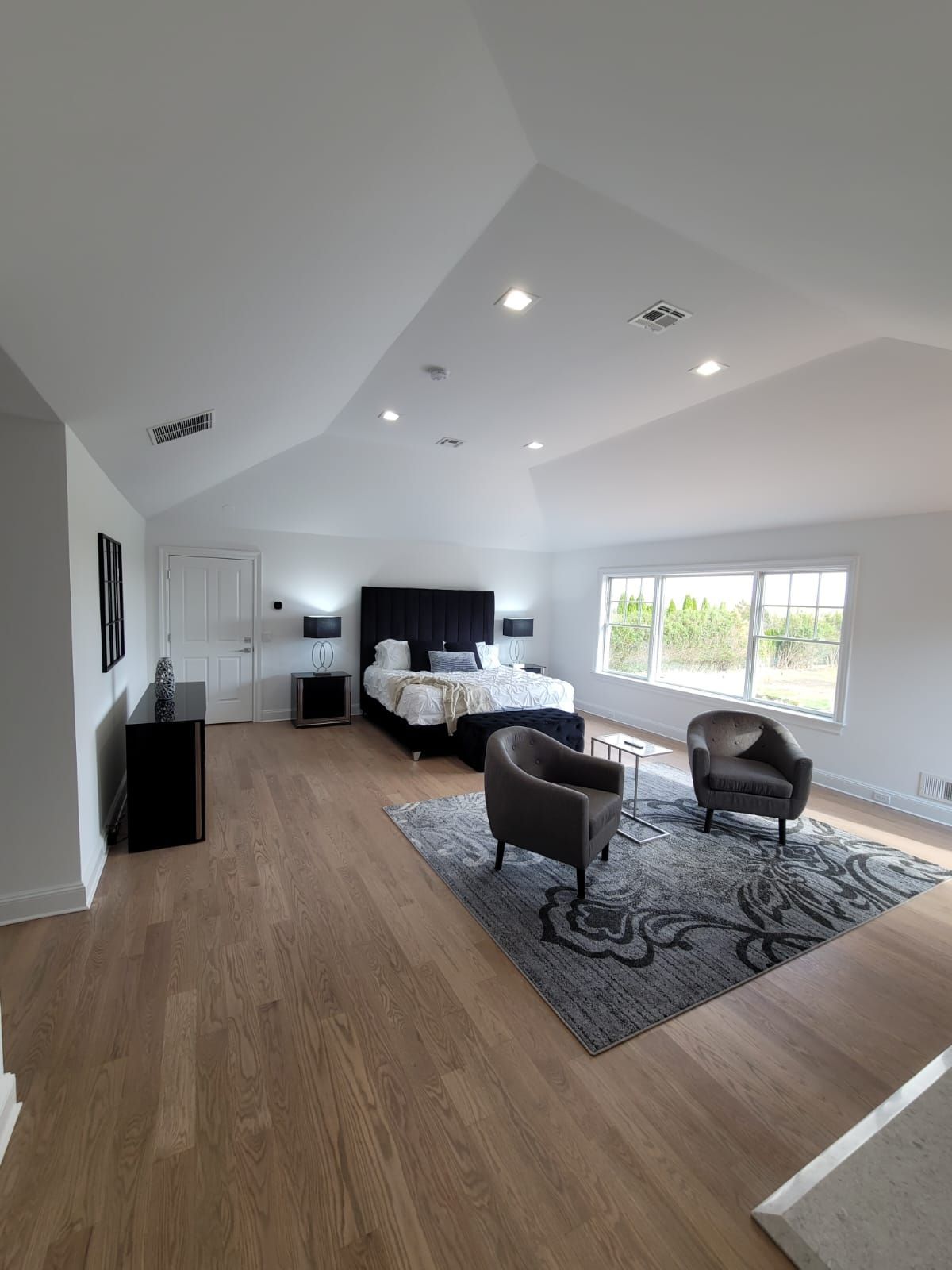 A large bedroom with a bed, chairs, and a rug.