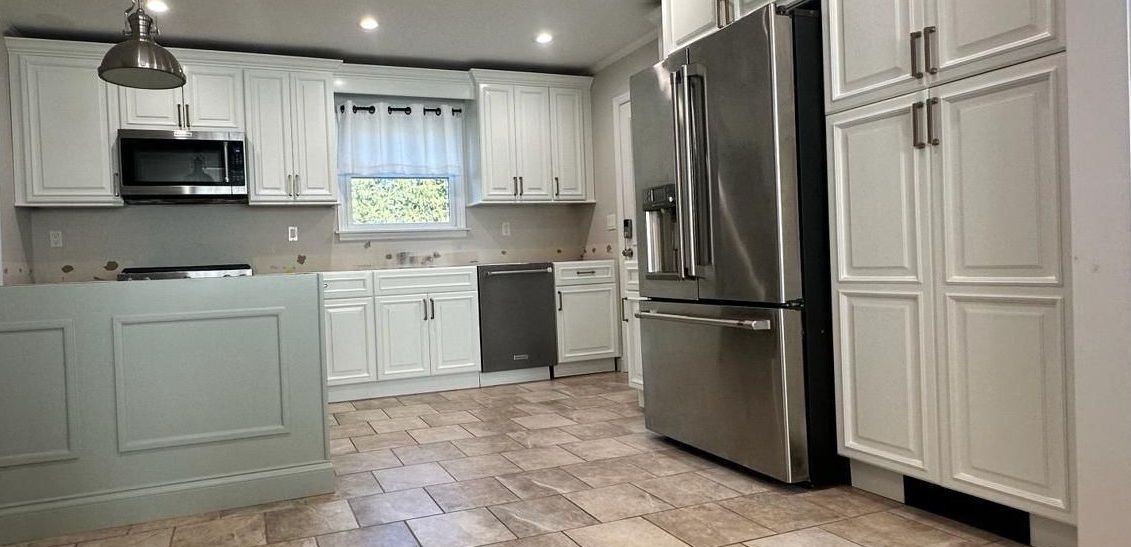 A kitchen with white cabinets, stainless steel appliances, a refrigerator and a wooden floor.
