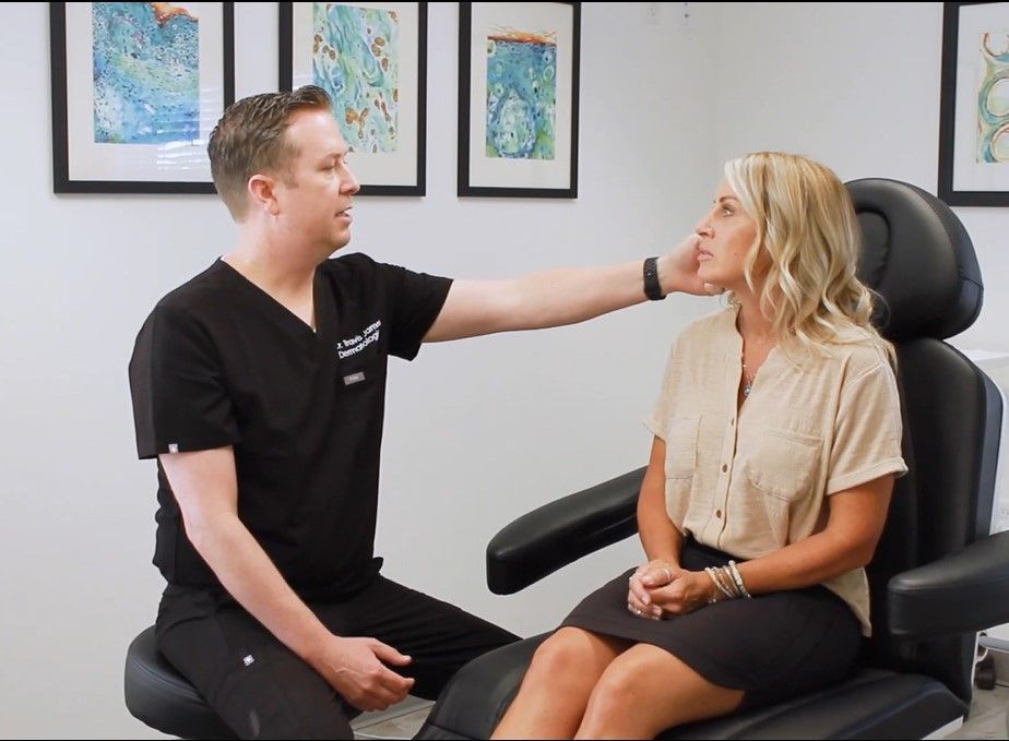 Clinician examining a seated patient in a bright office, with framed artwork on the wall.