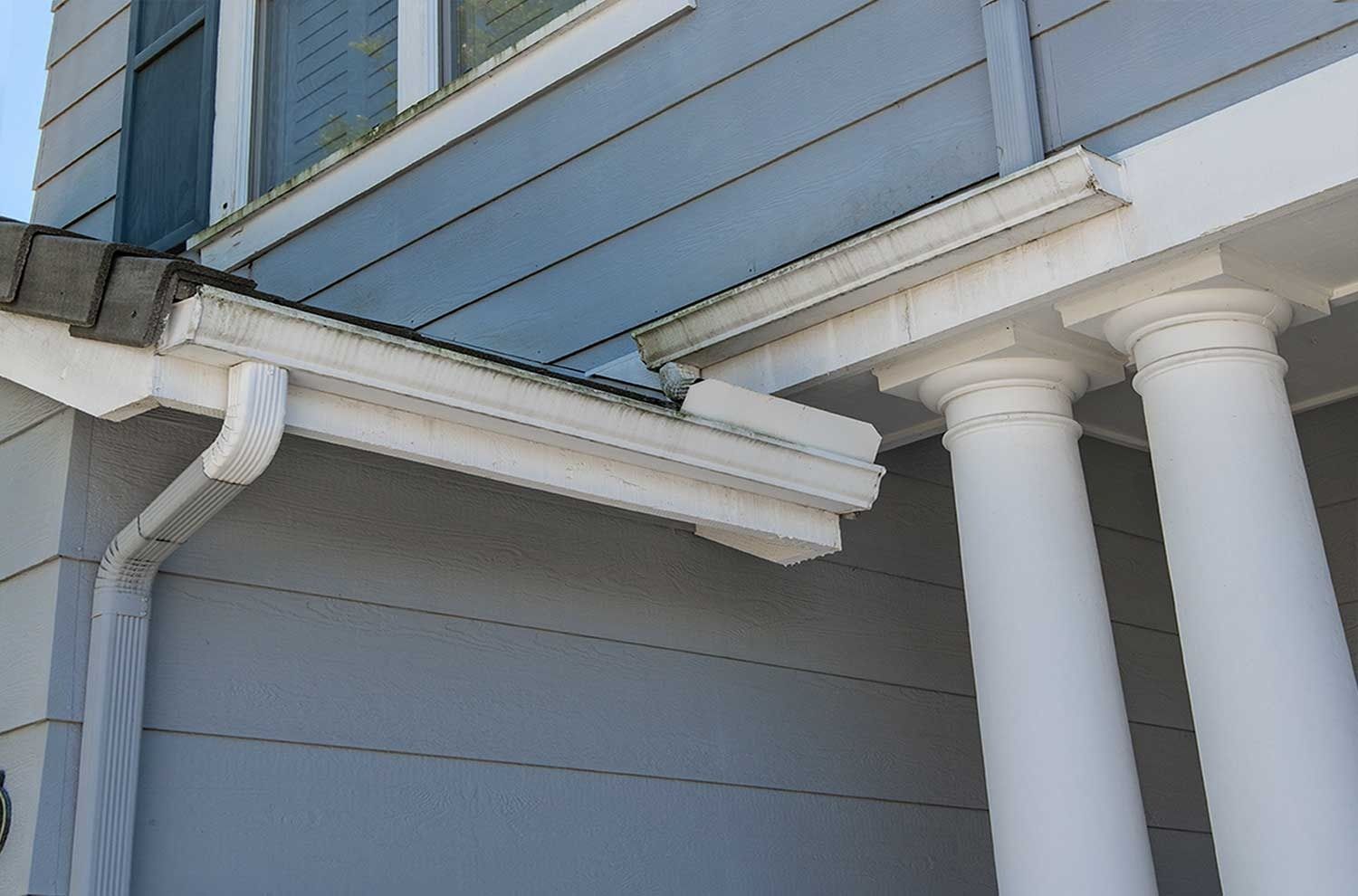 Exterior corner of a blue house with white trim and columns under the roofline