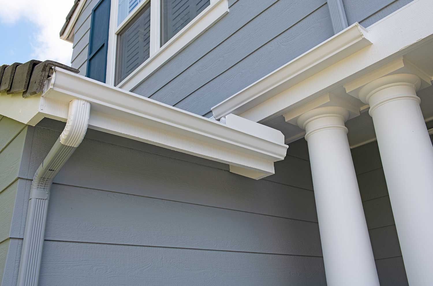 White columns and gray house siding with roof gutters on a home exterior