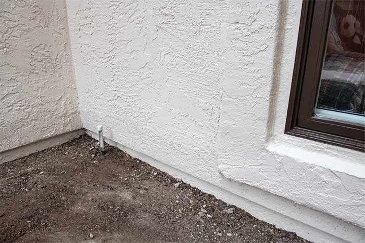 Exterior stucco wall corner with a small pipe and gravel ground beside a window