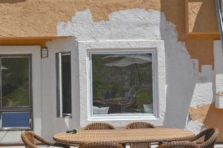 Patio with white-framed windows and wicker chairs around a round table against a tan stucco wall
