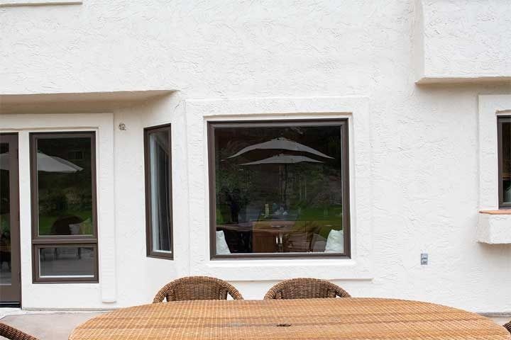 Patio outside white stucco house with glass doors and windows, wicker chairs, and a wooden table