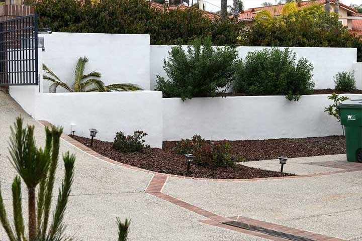 Curved driveway beside white retaining walls with green shrubs and potted plants