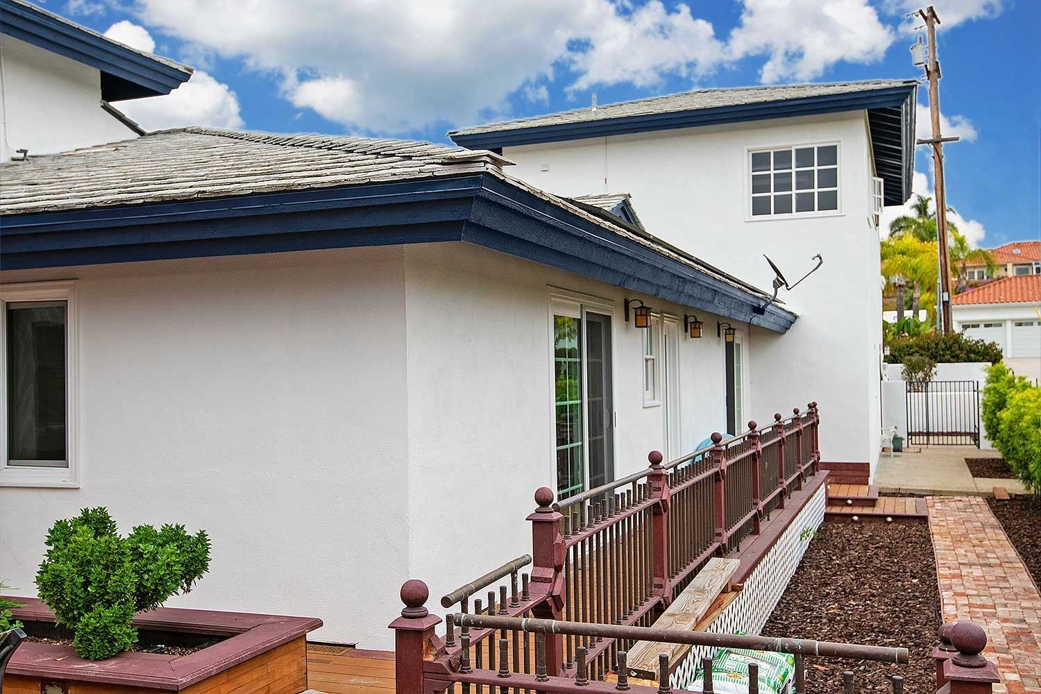 White house with blue roof trim beside a brick path and metal fence under a partly cloudy sky