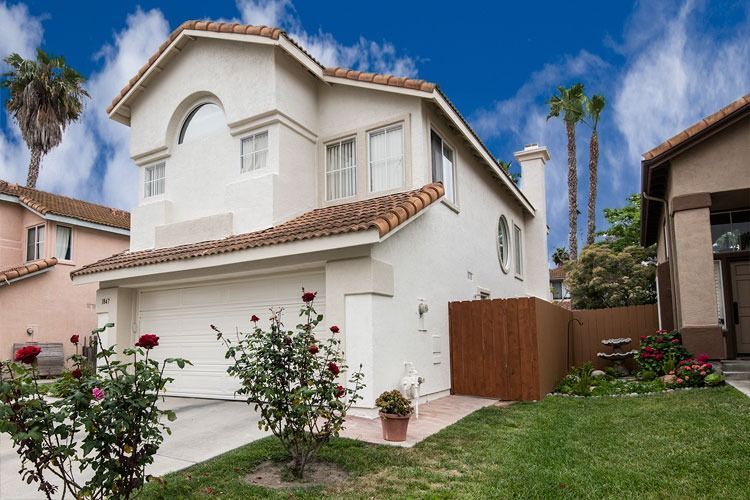 Two-story white house with red tile roof, front garden, and driveway under a blue sky