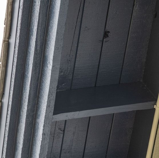 Close-up of black wooden boards and a shelf-like beam with a yellow pole at the right edge