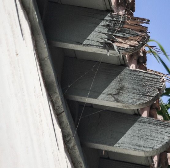 Tilted view of a concrete wall with triangular supports and rooftop debris under a blue sky