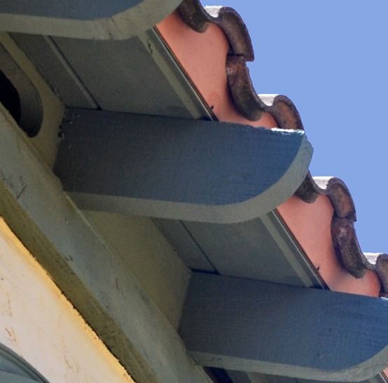 Blue-gray roof eaves with curved terracotta tiles against a clear blue sky