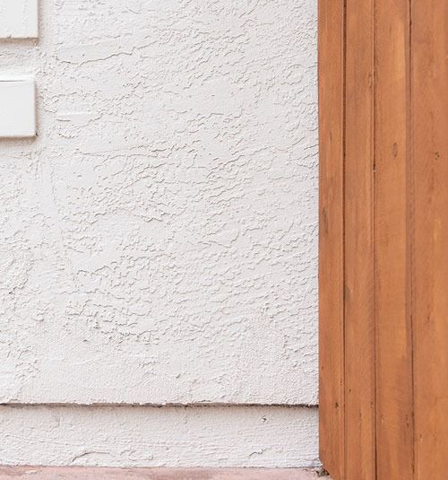 White stucco wall beside a vertical wooden door frame and a light switch on the left