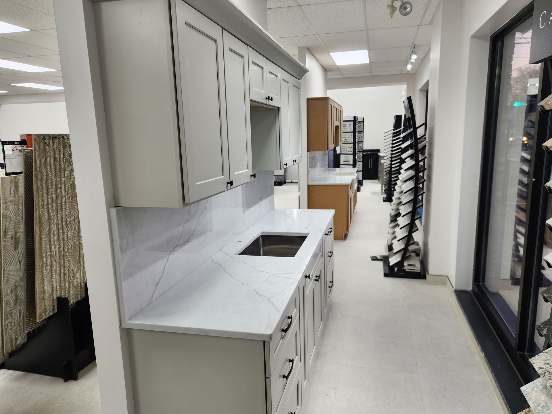 Kitchen showroom display with white cabinets, countertops, and gray backsplash