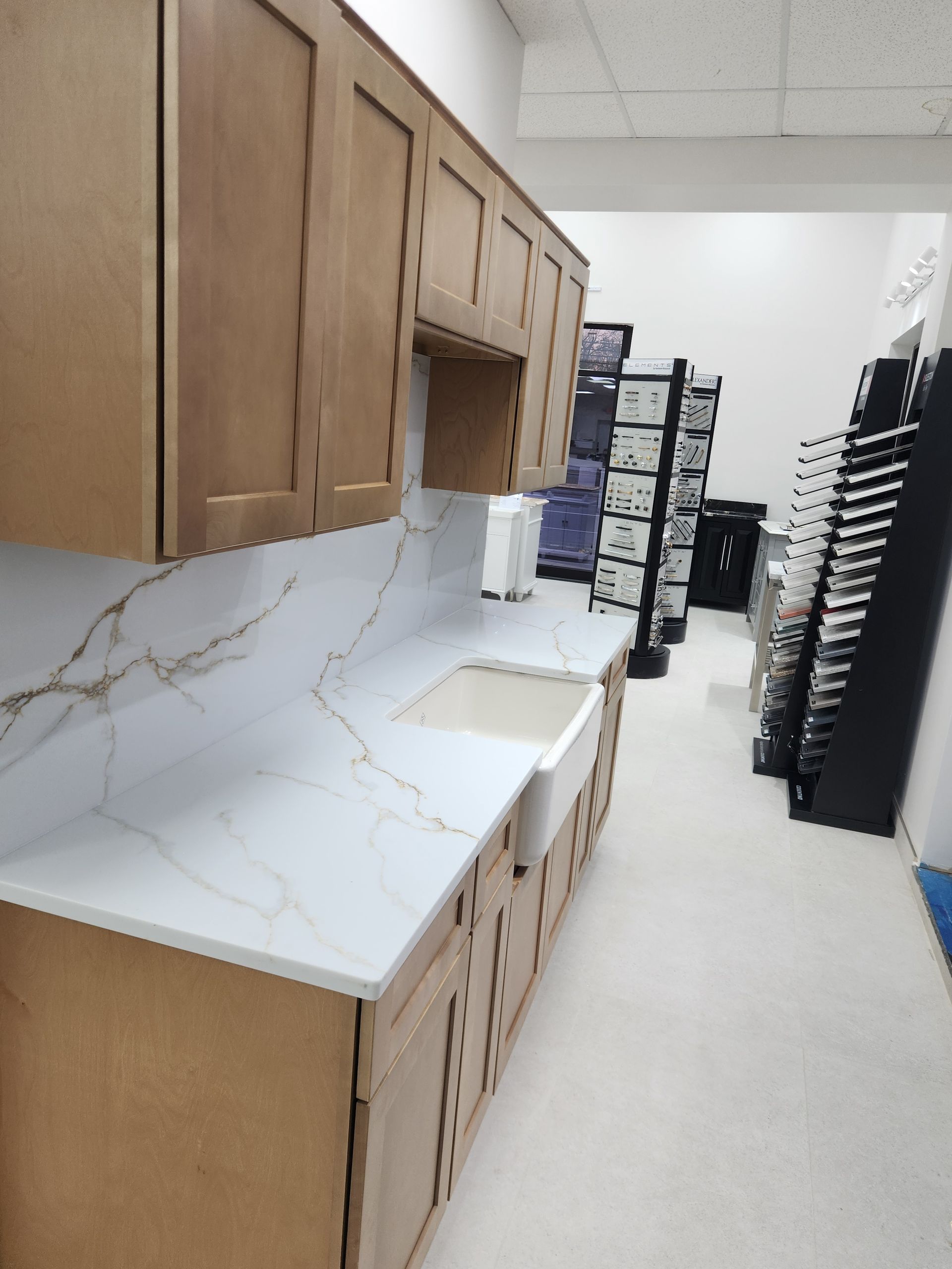 Kitchen display with light wood cabinets, white countertops with gold veining, and a white farmhouse sink