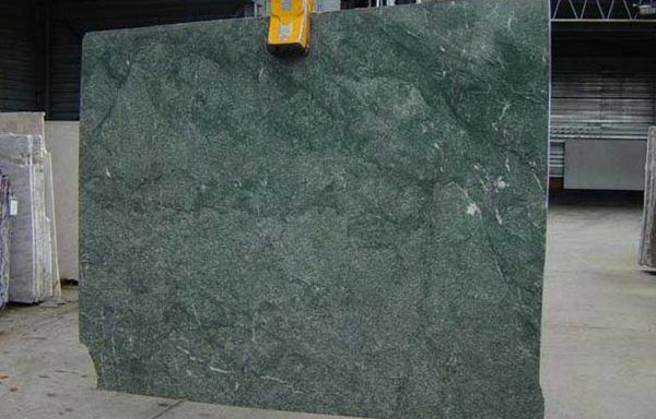 A large green marble slab is sitting on the ground in a warehouse.