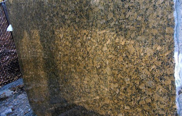 A large piece of granite is sitting on the ground in front of a fence.