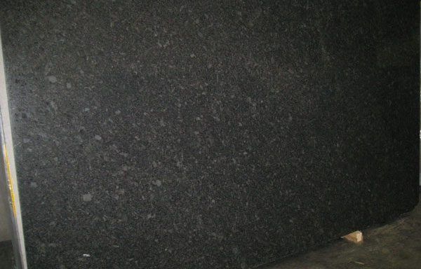 A large black granite slab is sitting on the floor next to a wall.