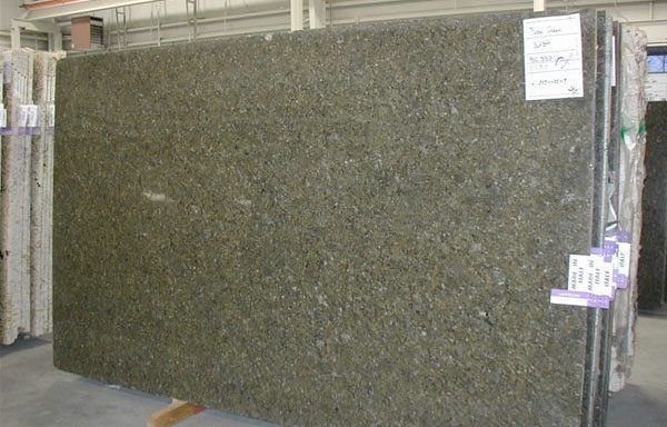A large green granite slab is sitting on a wooden pallet in a warehouse.