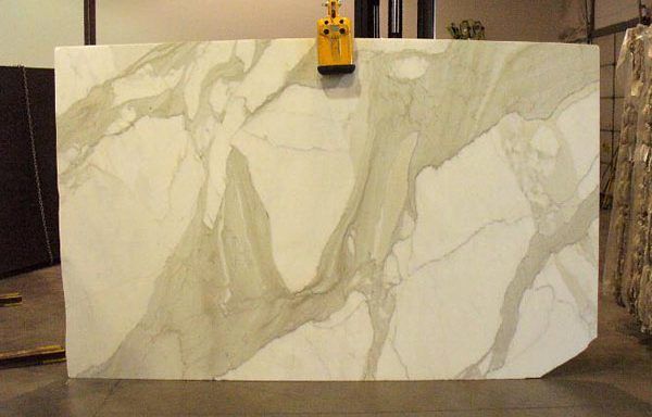 A large white marble slab is being lifted by a crane.