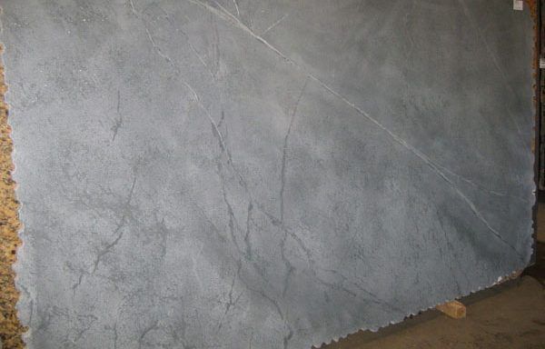 A large gray granite slab is sitting on the floor next to a wall.