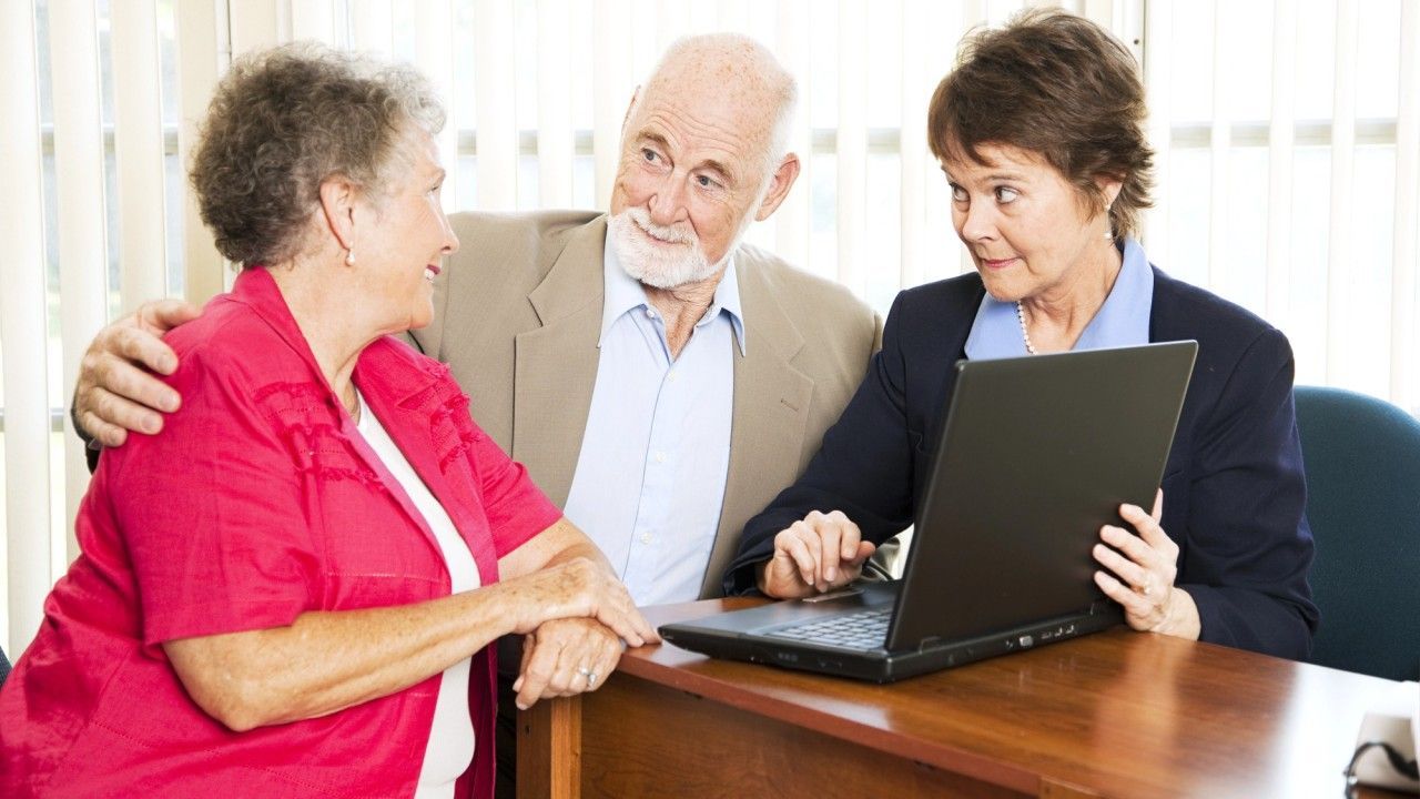 Woman shows laptop to older couple at a desk. The man has his arm around the woman.