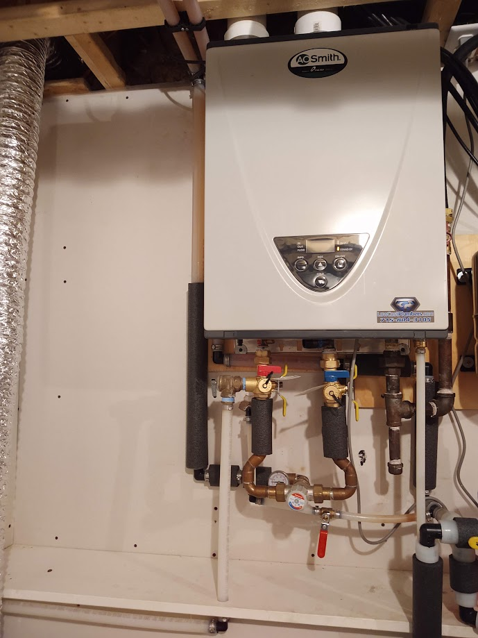 A white boiler is hanging on a wall in a basement.