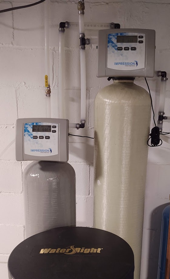 A water softener is sitting in a basement next to a wall.